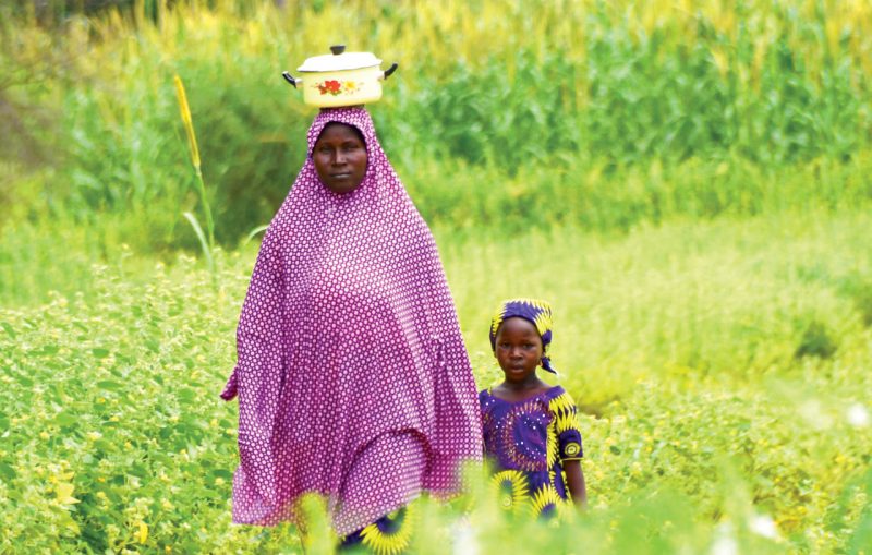 A woman and a girl standing in a lush field in Africa