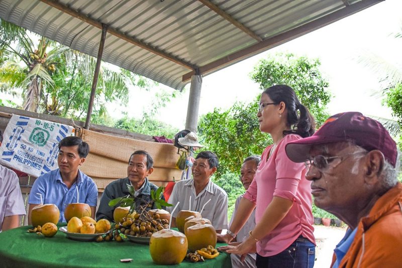 Hanh Tran (standing) speaks to a group of longan farmers in Vietnam about integrated pest management techniques for the fruit. They were joined by Muni Muniappan (right), director of the Feed the Future Innovation Lab for Integrated Pest Management.