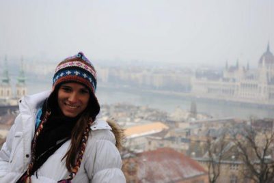 a woman in a winter hat stand in front of a wintery cityscape
